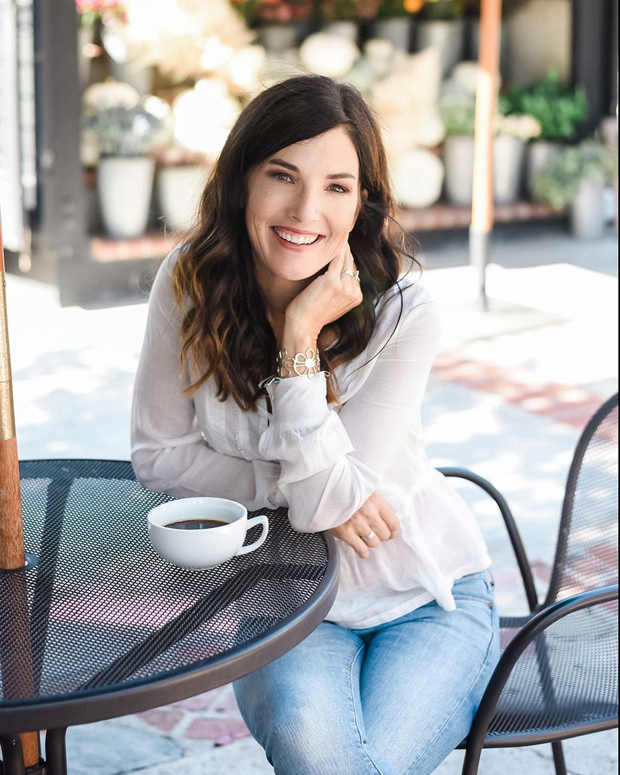 A woman is sitting at a table with a cup of coffee.
