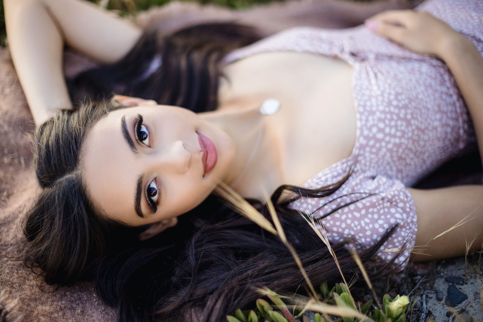 Woman lying on grass in a pink dress, gazing at the camera with a calm expression.