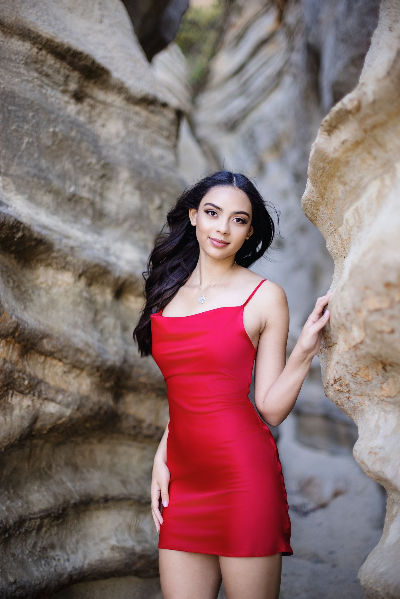 Woman in a red dress posing between large rock formations outdoors.