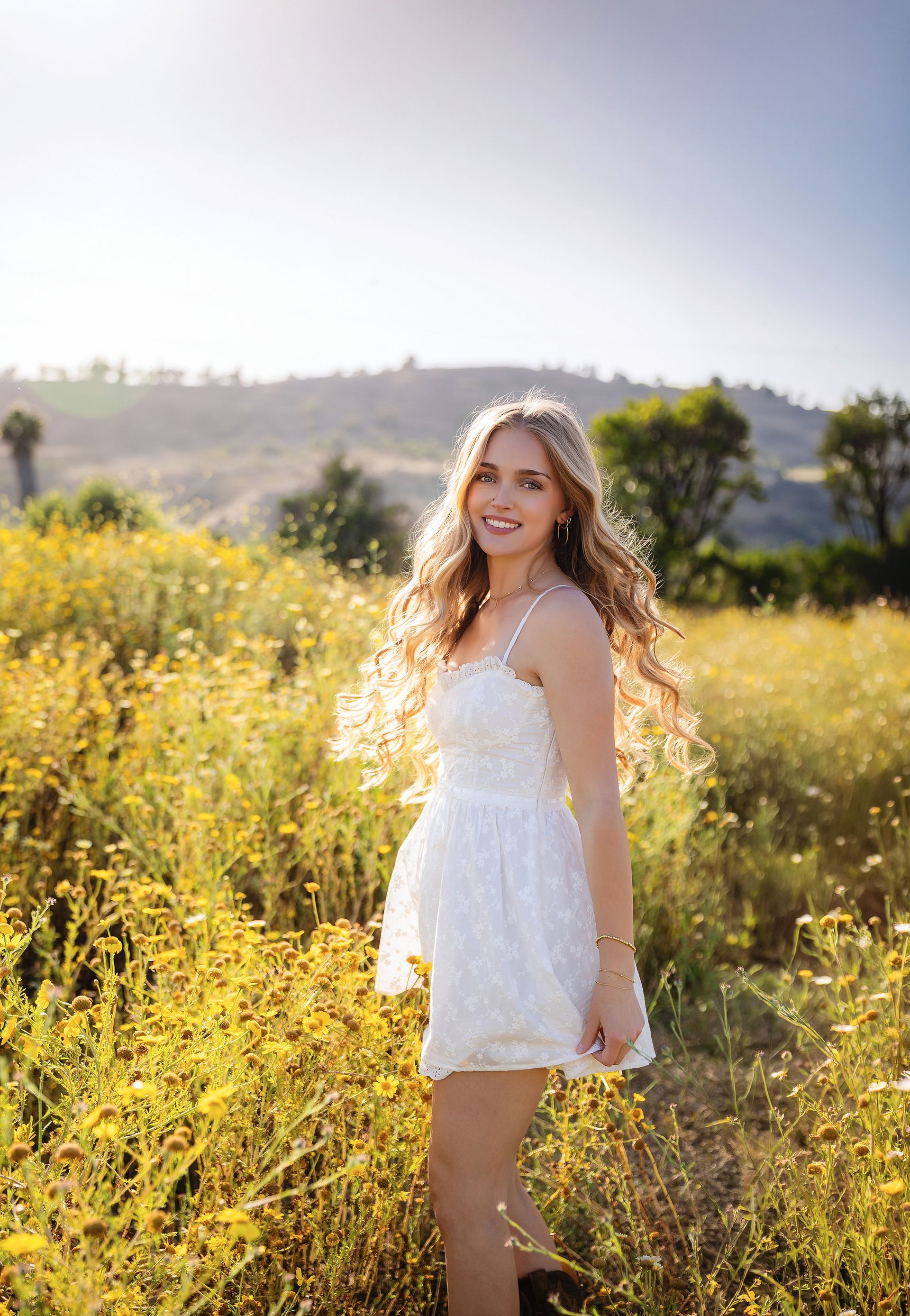 Senior girl in a white dress in a field of yellow wildflowers in San Juan Capistrano open space