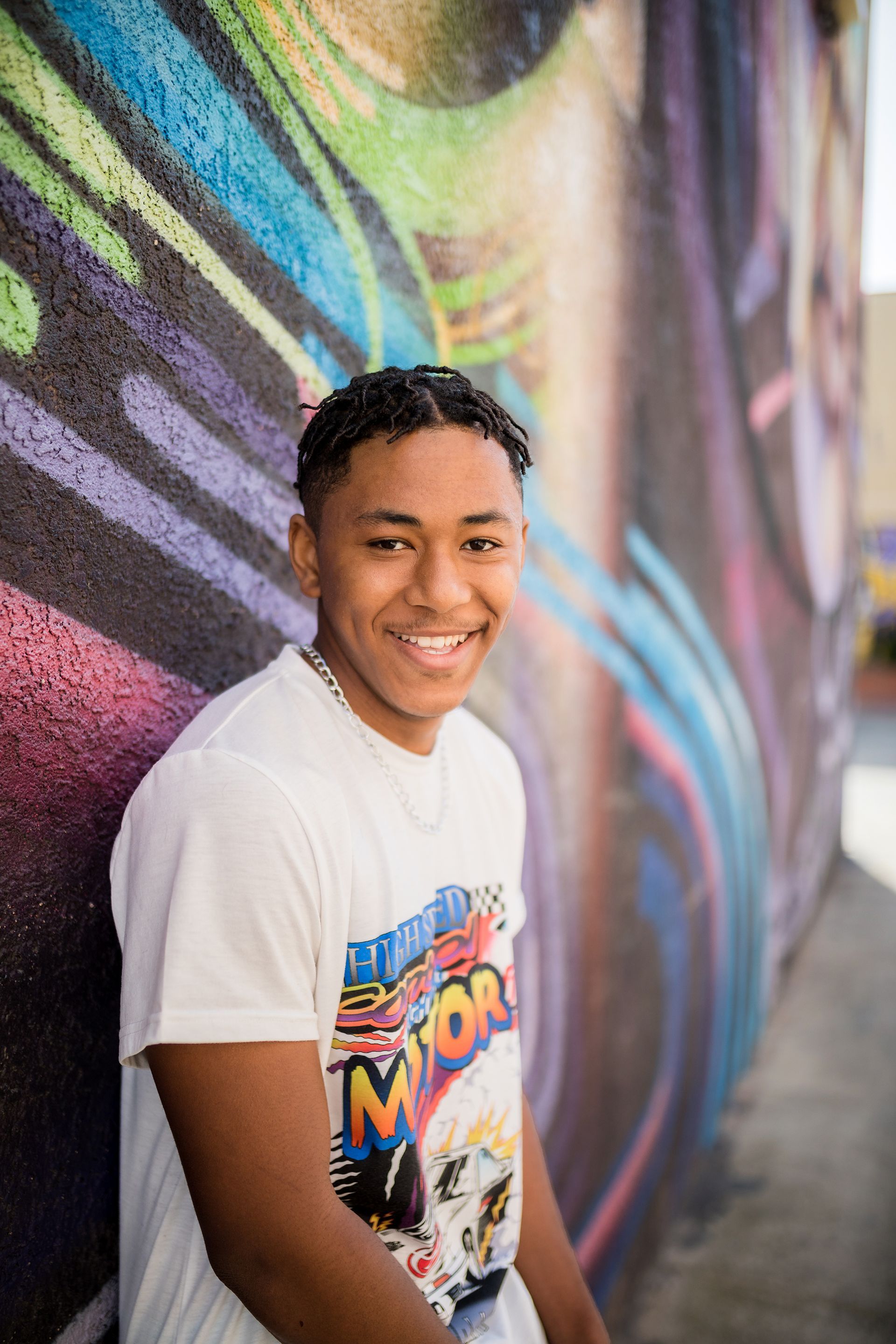 A young man is standing in front of a colorful graffiti wall.