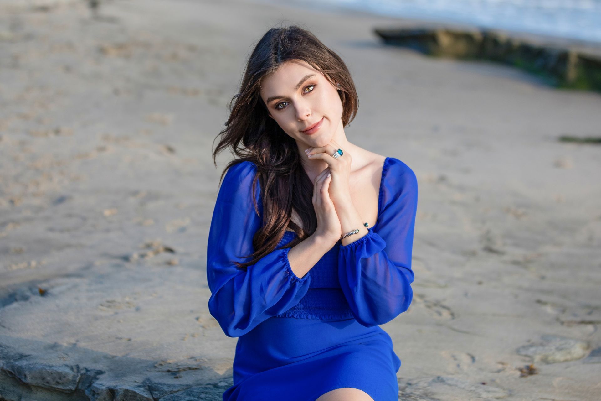 A woman in a blue dress is sitting on the beach.