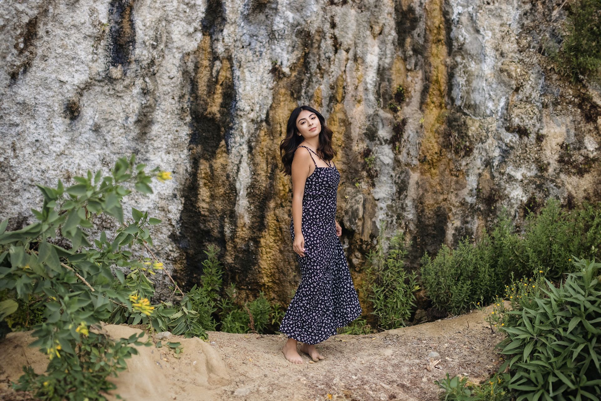 A woman in a dress is standing in front of a rock wall.