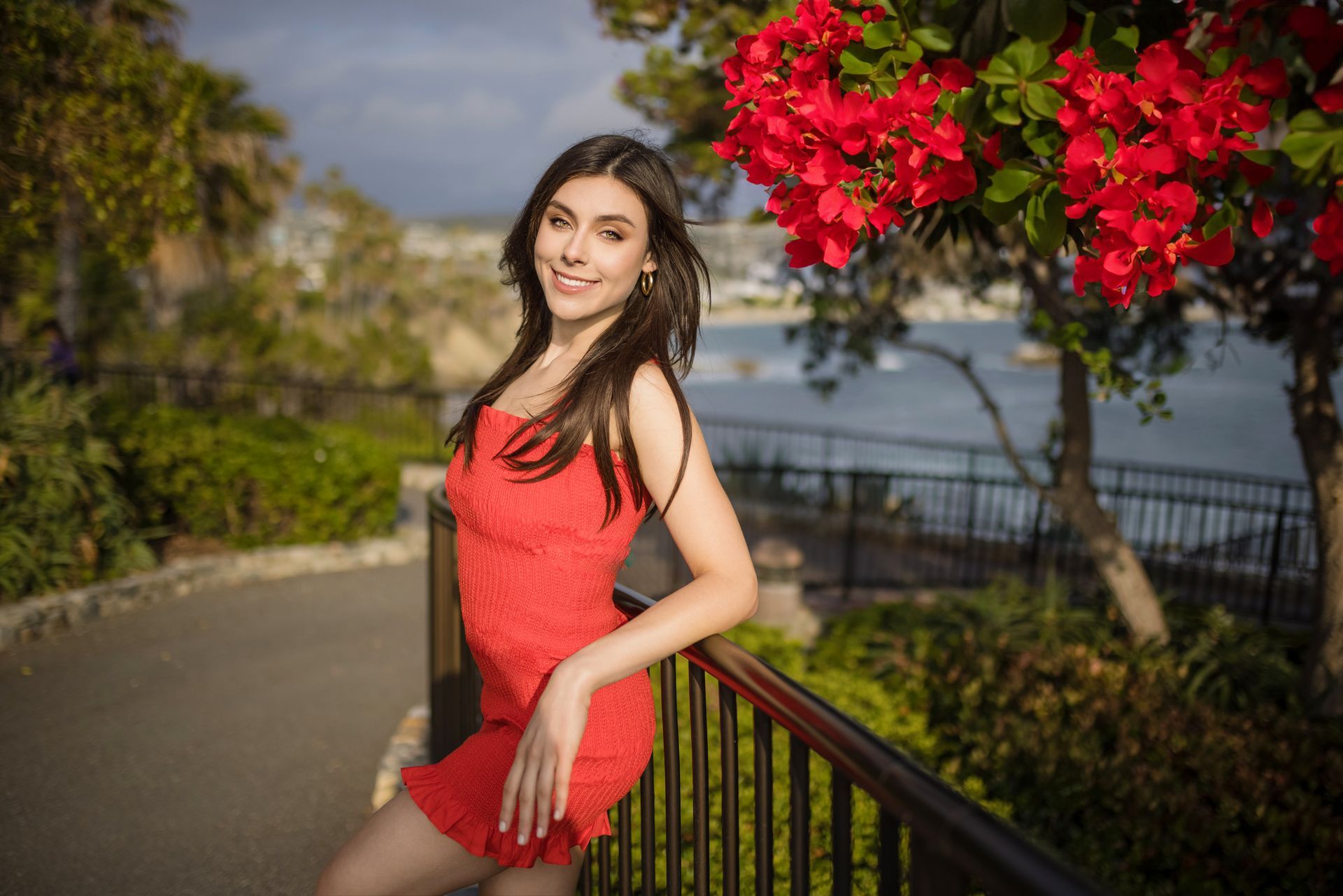 A woman in a red dress is standing next to a railing in a park.