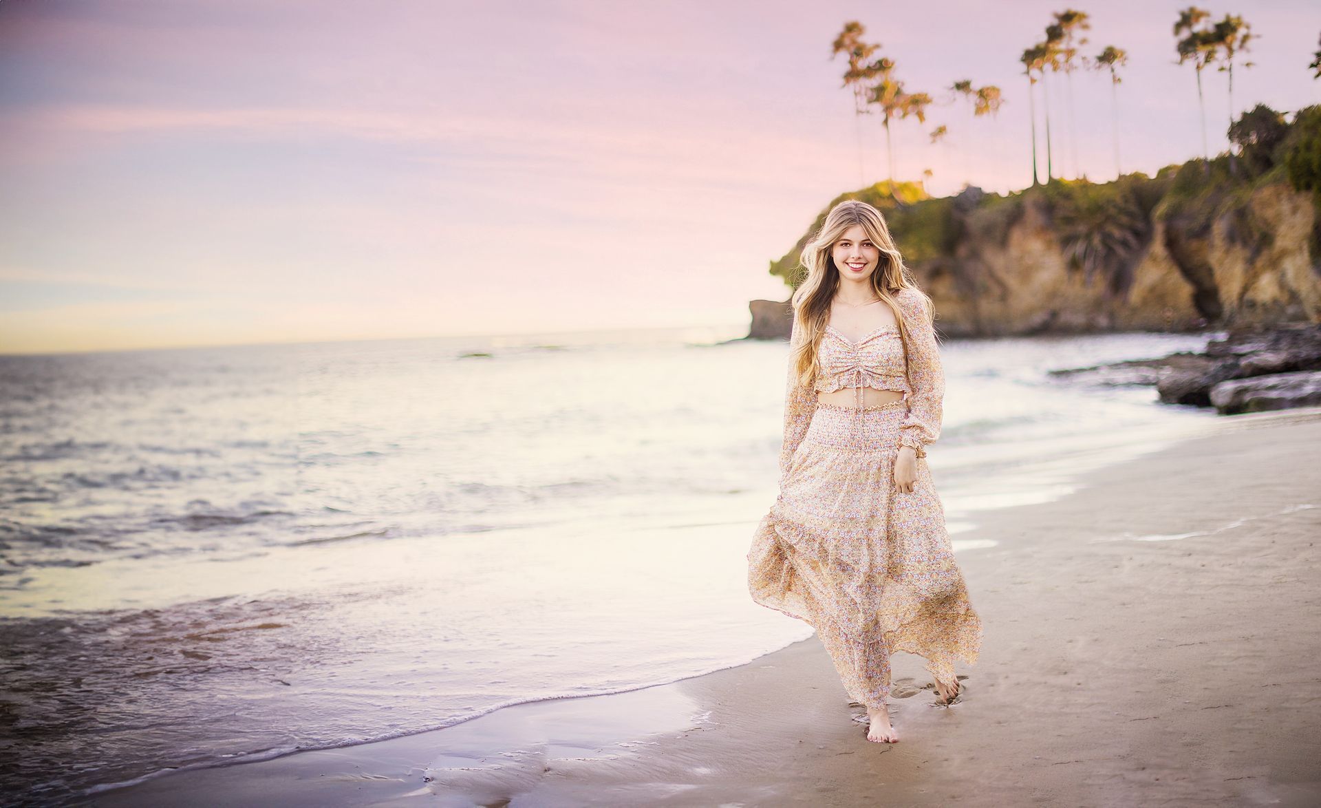 A woman in a long dress is walking on the beach.