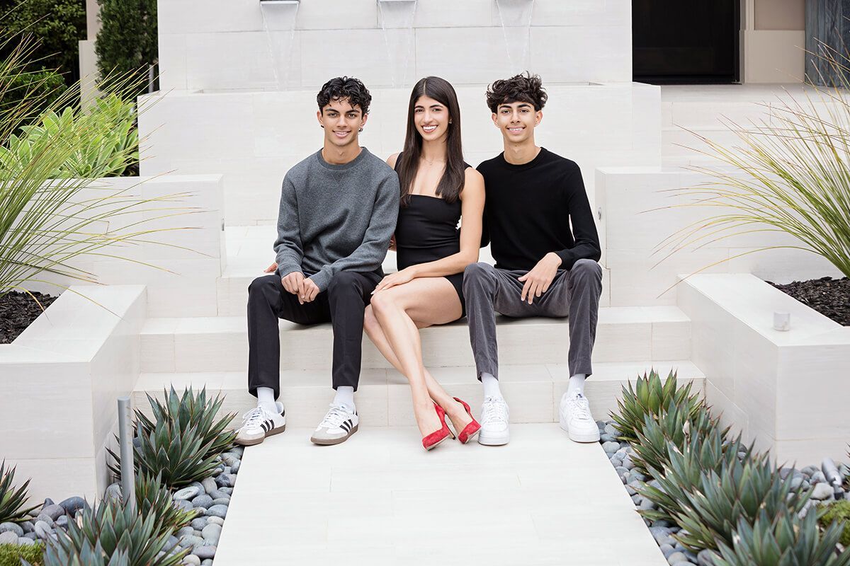 Stylish sibling trio seated in a modern garden courtyard, captured during a luxury sibling photography session in Newport Beach by Orange County photographer Blue Sky’s Studio.