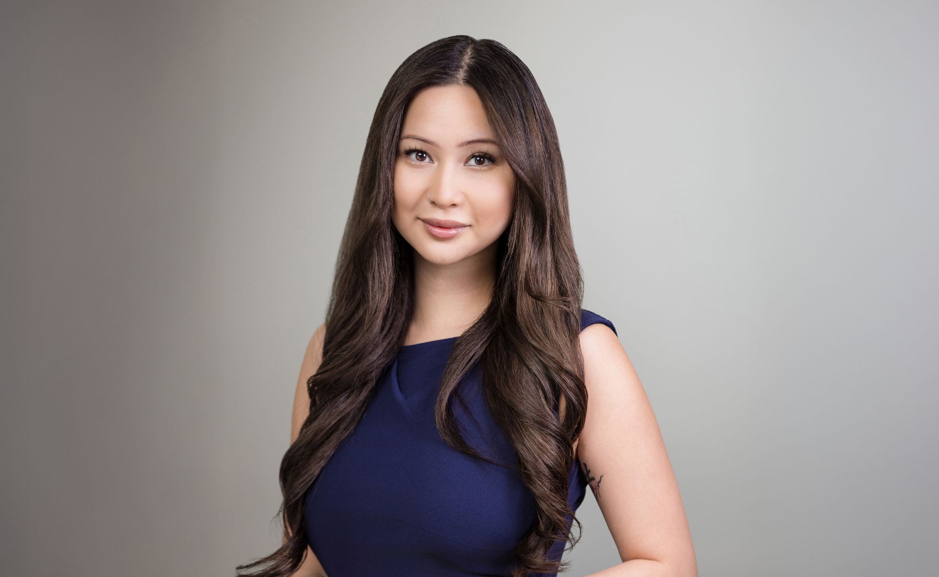 A woman in a blue dress is standing in front of a gray background.