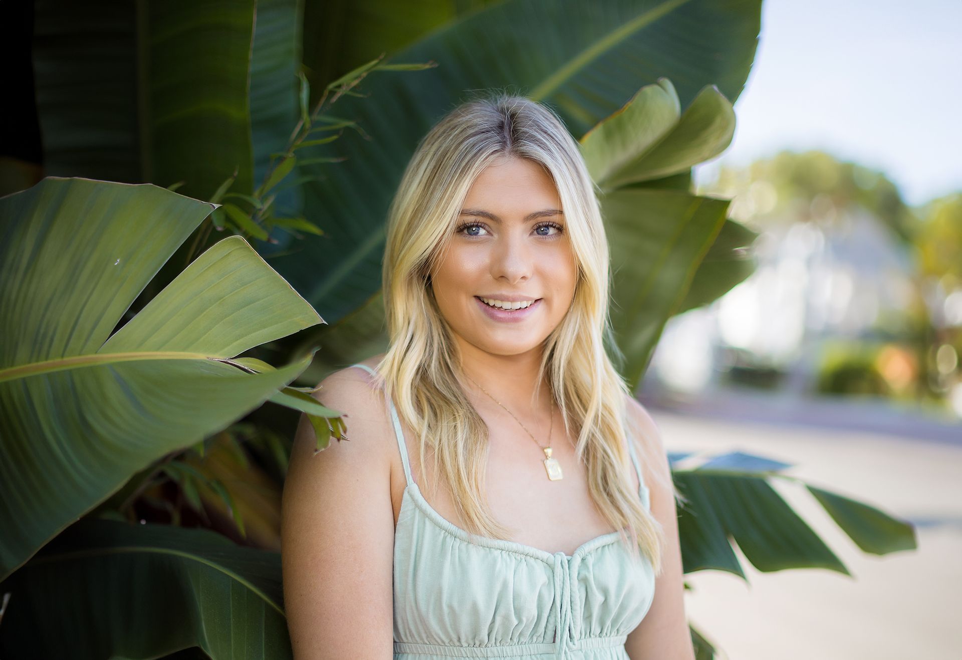A woman in a green dress is standing in front of a palm tree.