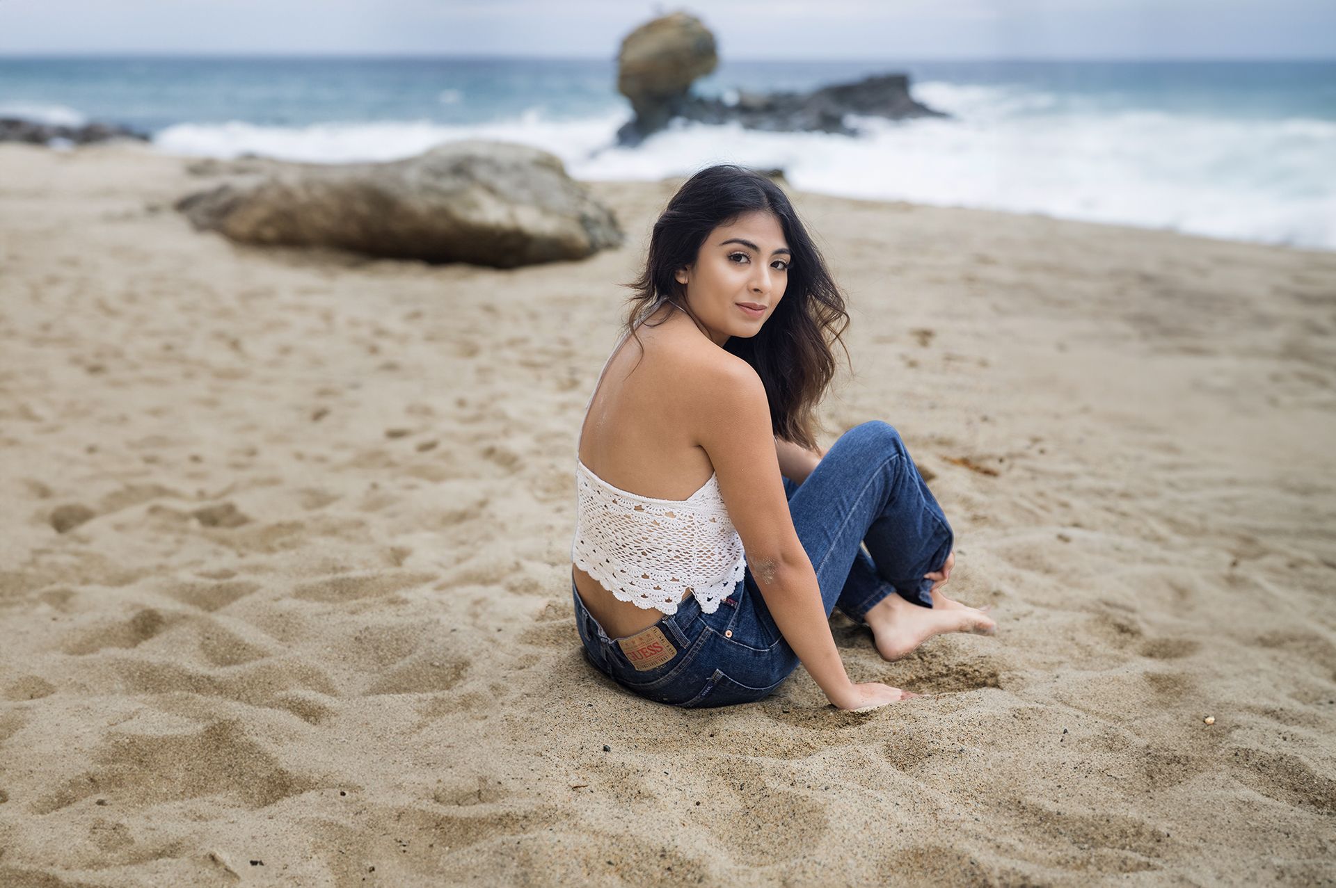 A woman is sitting on the beach with her legs crossed.
