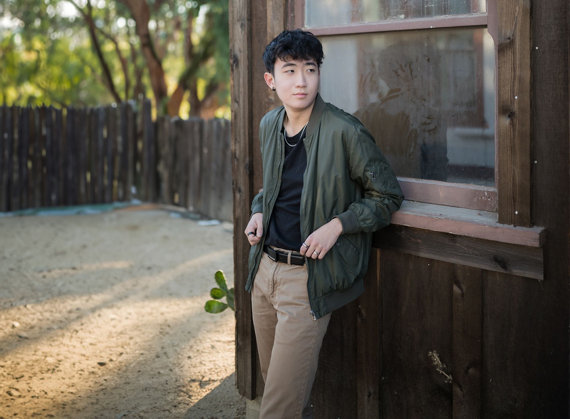 A young man in a green jacket is leaning against a wooden wall.