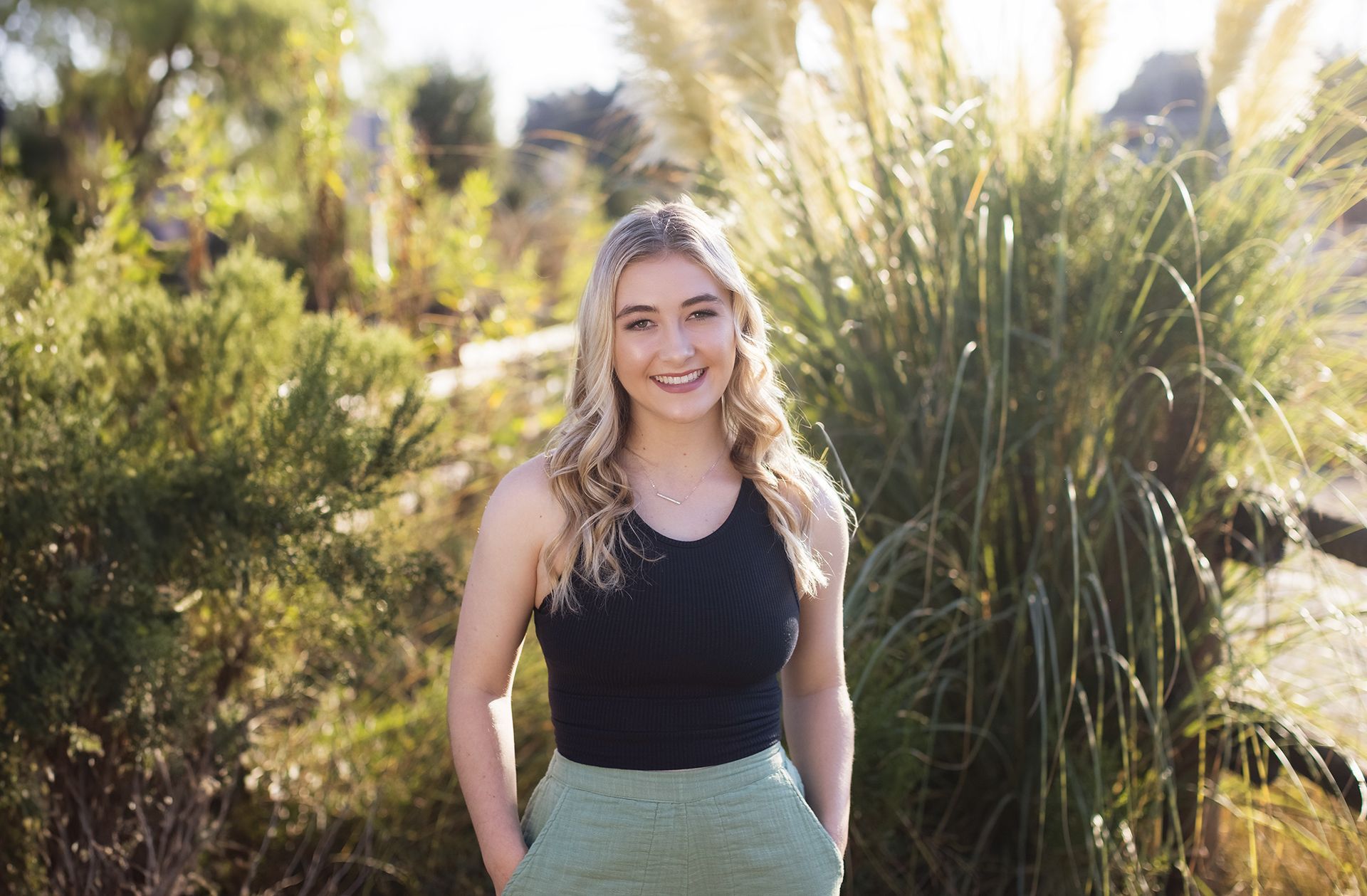 A woman in a black tank top and green skirt is standing in front of tall grass.