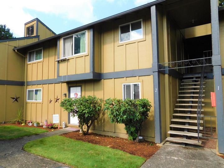 Two-story apartment building with tan siding, gray trim, and outdoor stairs.