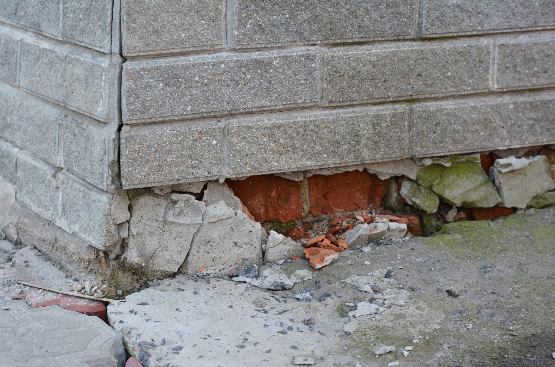 Cracked brick foundation with crumbling concrete and exposed red bricks near the corner of a wall