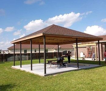 Covered outdoor pavilion with picnic tables on a grassy lawn under a blue sky