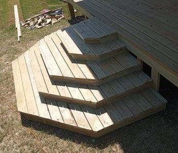 Wooden hexagonal staircase leading to a raised deck on grass under a house overhang
