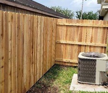 Wooden privacy fence enclosing a small yard with an outdoor air conditioner unit on a concrete pad.