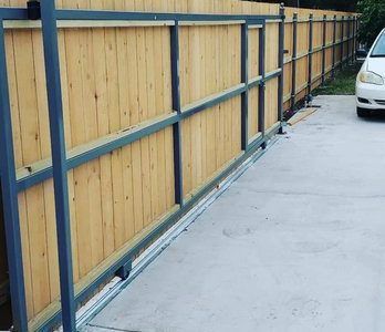 Wooden fence with blue metal rails along a concrete driveway beside a parked white car