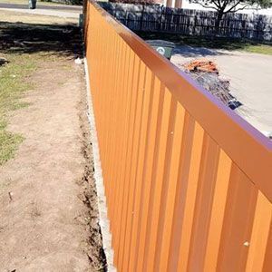 Orange metal fence along a dirt path beside a paved area on a sunny day