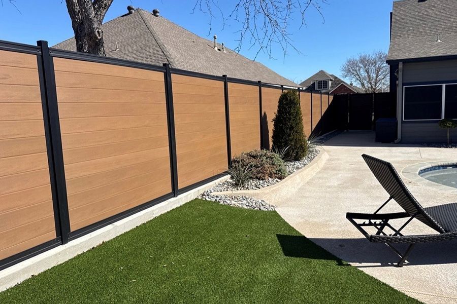 Backyard with green lawn, tan privacy fence, patio, and a reclining chair in bright sunlight