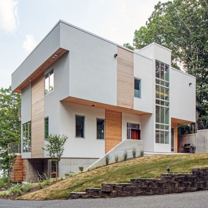 Modern white two-story house with wood accents on a sloped, landscaped lot