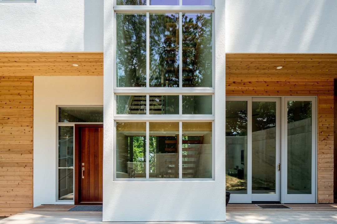 Modern house exterior with large white-framed windows, wood siding, and glass sliding doors