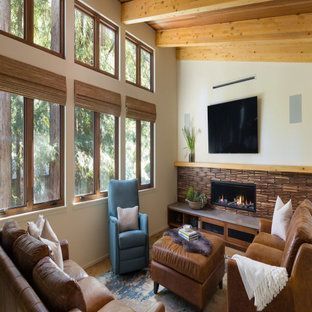 Cozy living room with tall windows, fireplace, wood ceiling, and brown and blue chairs around an ottoman