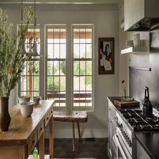 Bright kitchen with tall windows, wooden table, gas stove, and a vase of branches on the counter