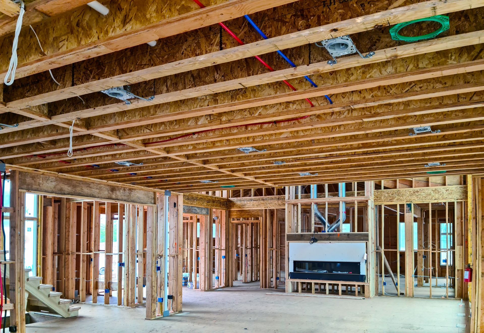 Interior of a framed house under construction with exposed wooden beams, studs, and unfinished floors and ceiling.