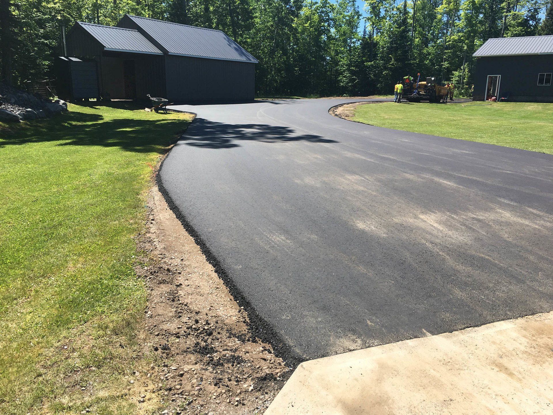 A newly paved driveway is surrounded by grass and trees.