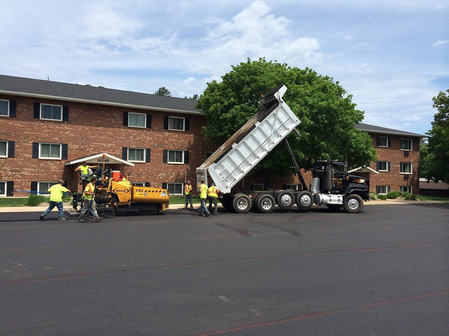 A dump truck is being loaded with asphalt in front of a brick building.