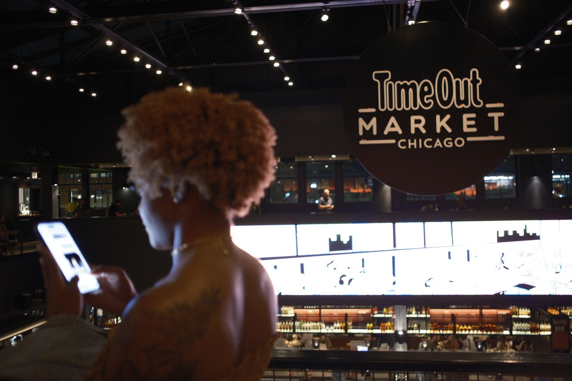 A woman is looking at her phone in front of a TimeOut Market Chicago sign