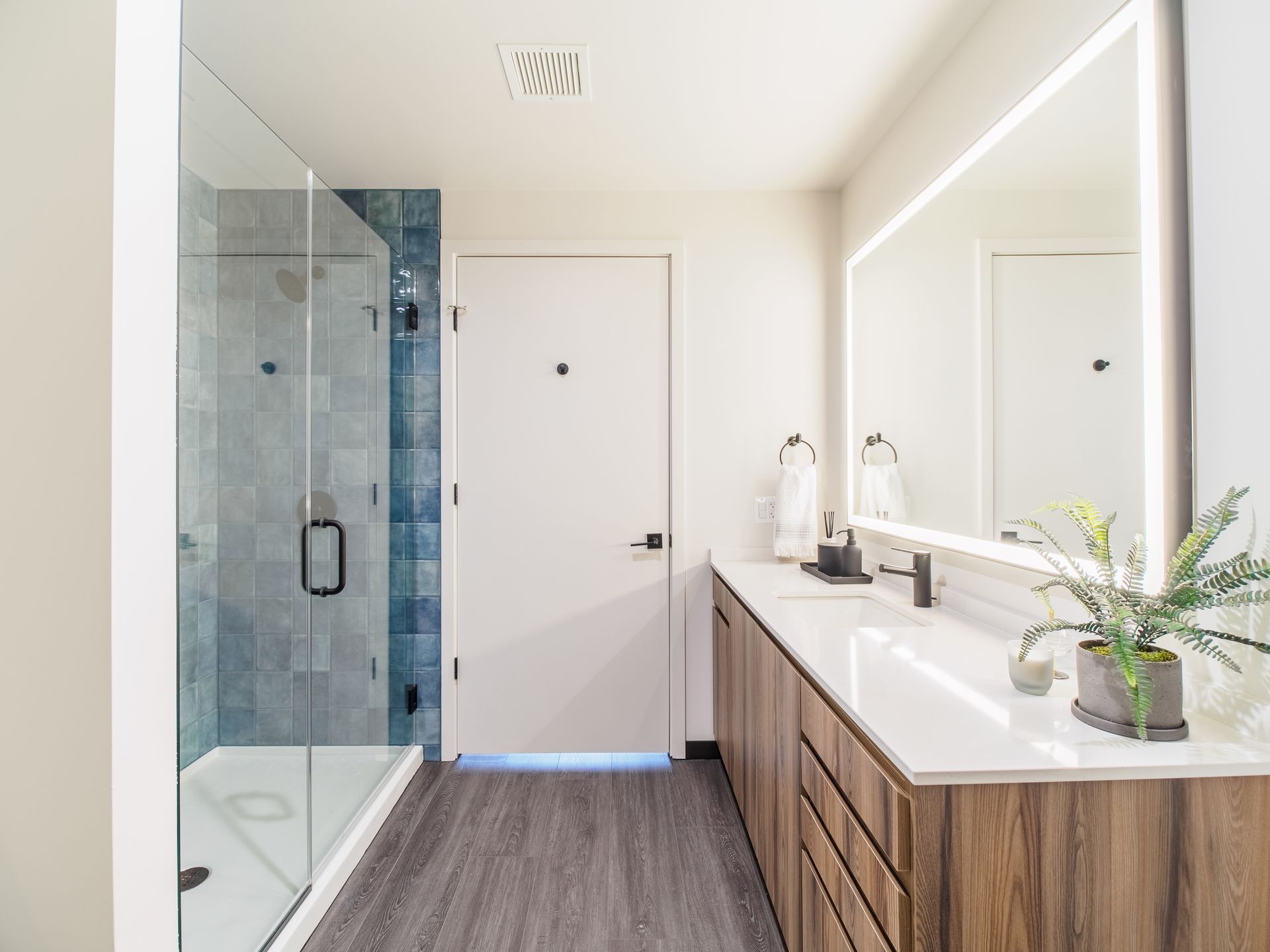 A bathroom with a sink , mirror and walk in shower.