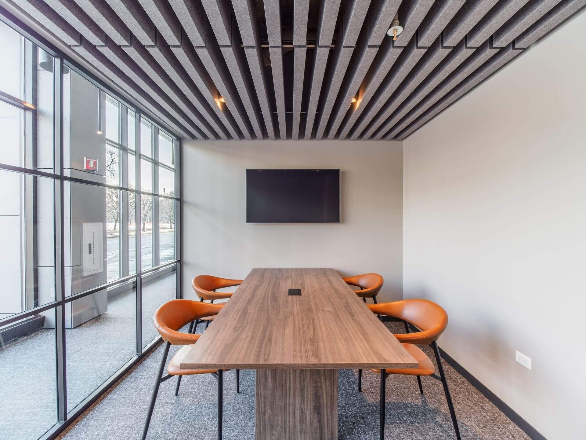 conference room with a long wood table, four orange chairs, and a mounted TV