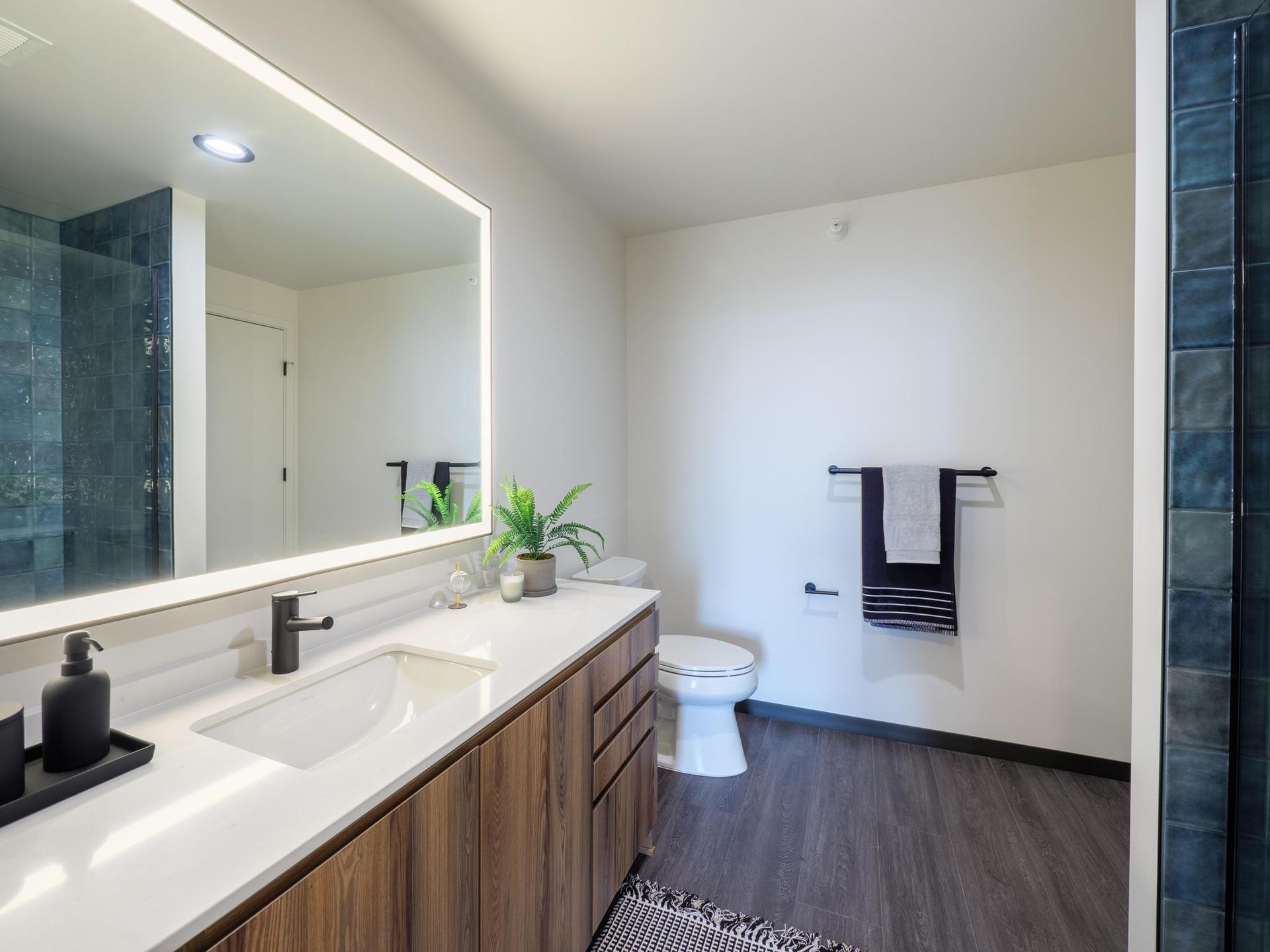 The Thompson at Fulton Market luxury apartment bathroom with an LED mirror, spacious vanity, and blue-tiled shower
