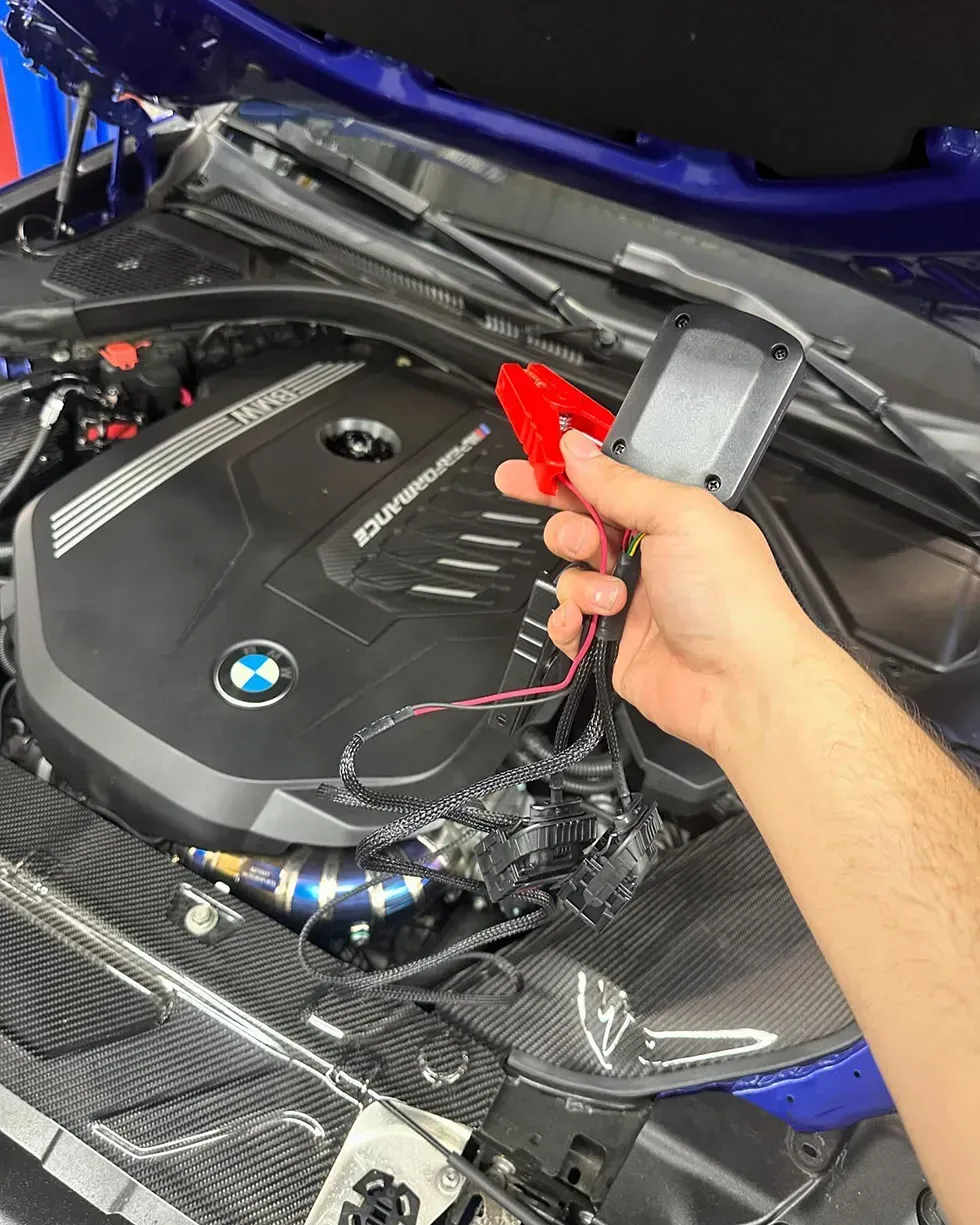 A person is holding a red jump starter under the hood of a car.
