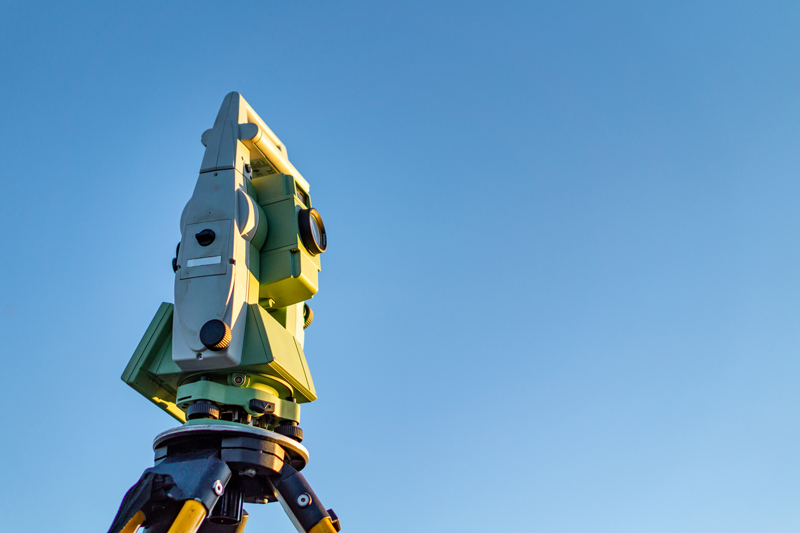 A theodolite is sitting on top of a tripod against a blue sky.