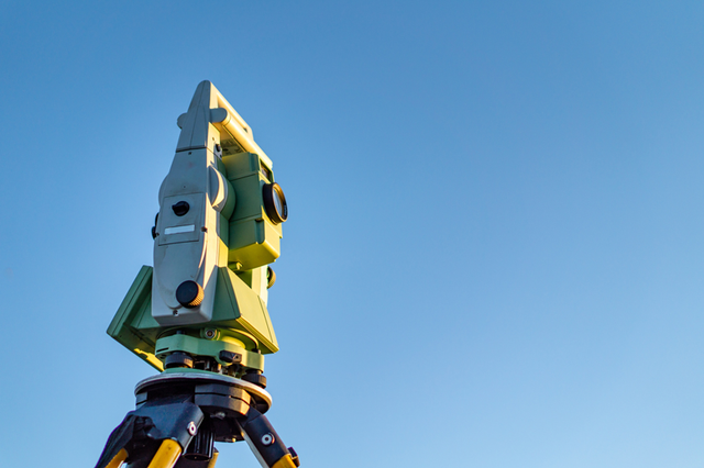 A theodolite is sitting on top of a tripod against a blue sky.