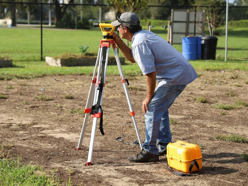 A man is using a level on a tripod in a field.