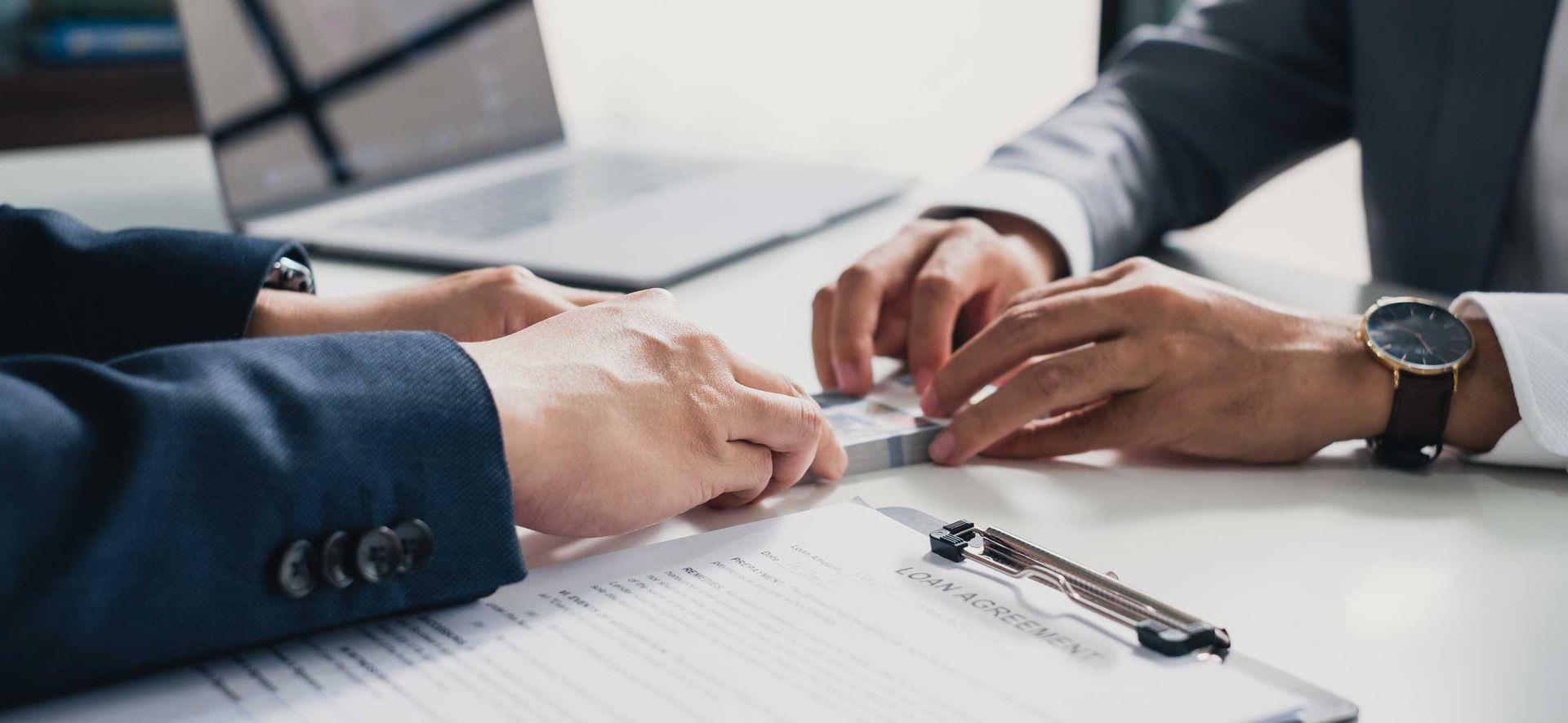 Two people in business suits discussing papers and signing a document at a table Two people in business suits discussing papers and signing a document at a table