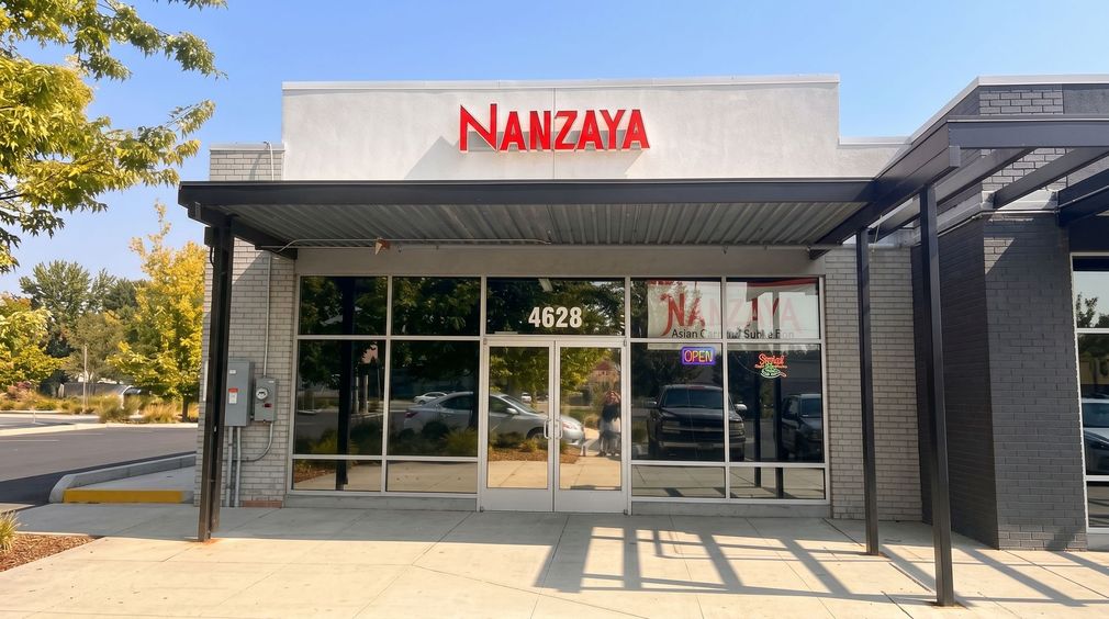 Storefront of Nanzaya with glass doors, red sign, and shaded entrance in a sunny plaza.