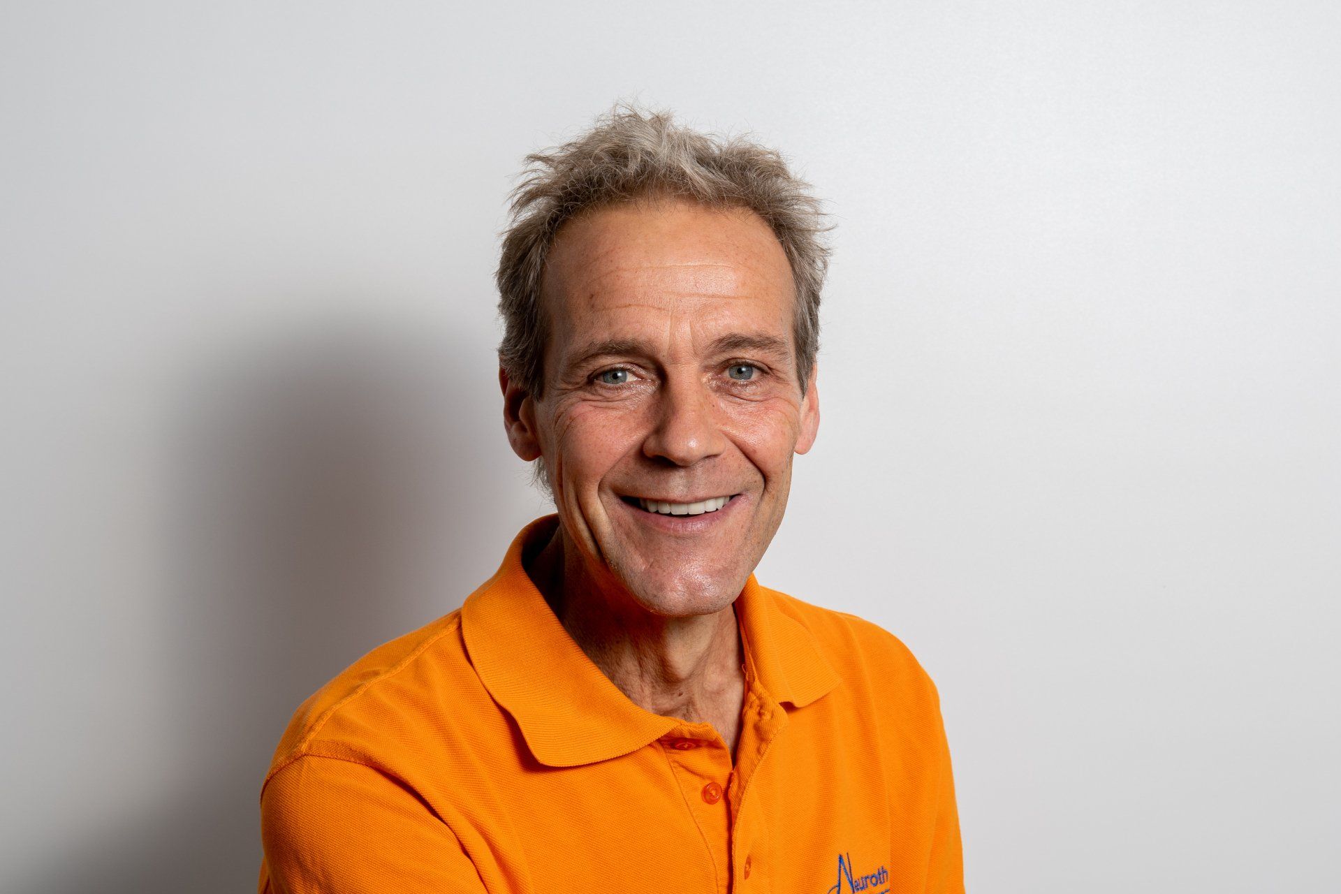 Ein Mann in einem orangefarbenen Poloshirt lächelt in die Kamera.