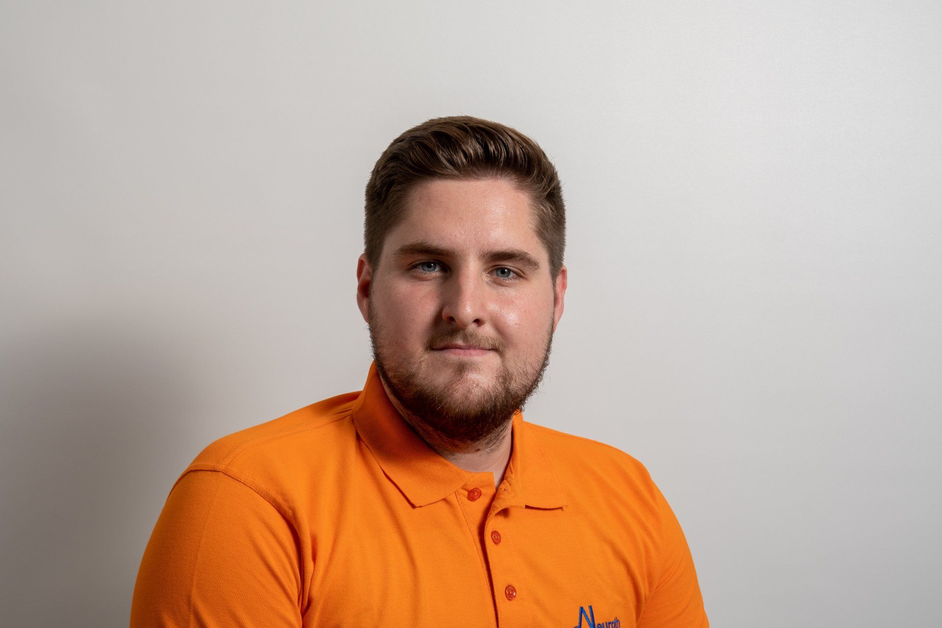 Ein Mann mit Bart trägt ein orangefarbenes Poloshirt.
