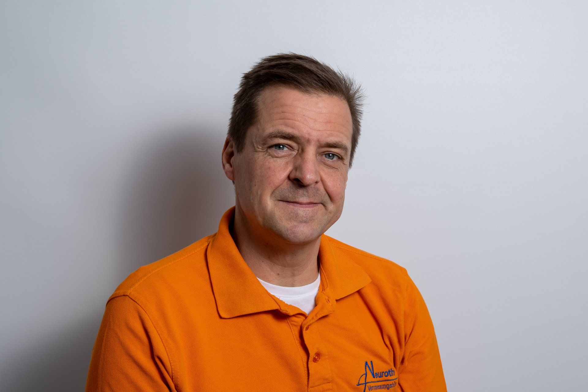 Ein Mann in einem orangefarbenen Poloshirt lächelt in die Kamera.