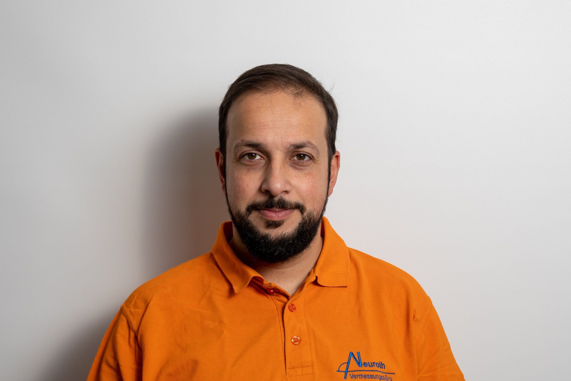 Ein Mann mit Bart trägt ein orangefarbenes Poloshirt.