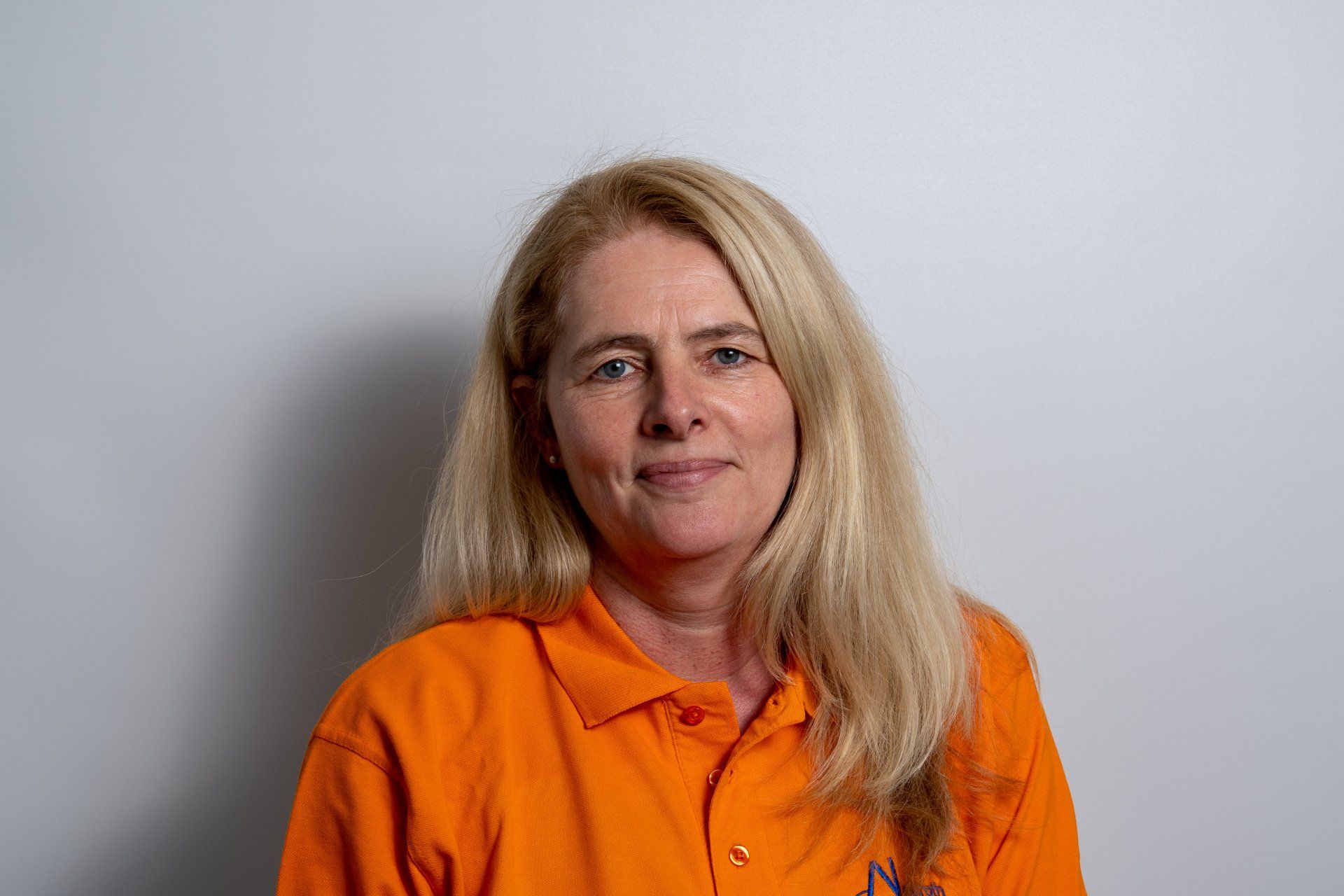Eine Frau trägt ein orangefarbenes Hemd und lächelt in die Kamera.