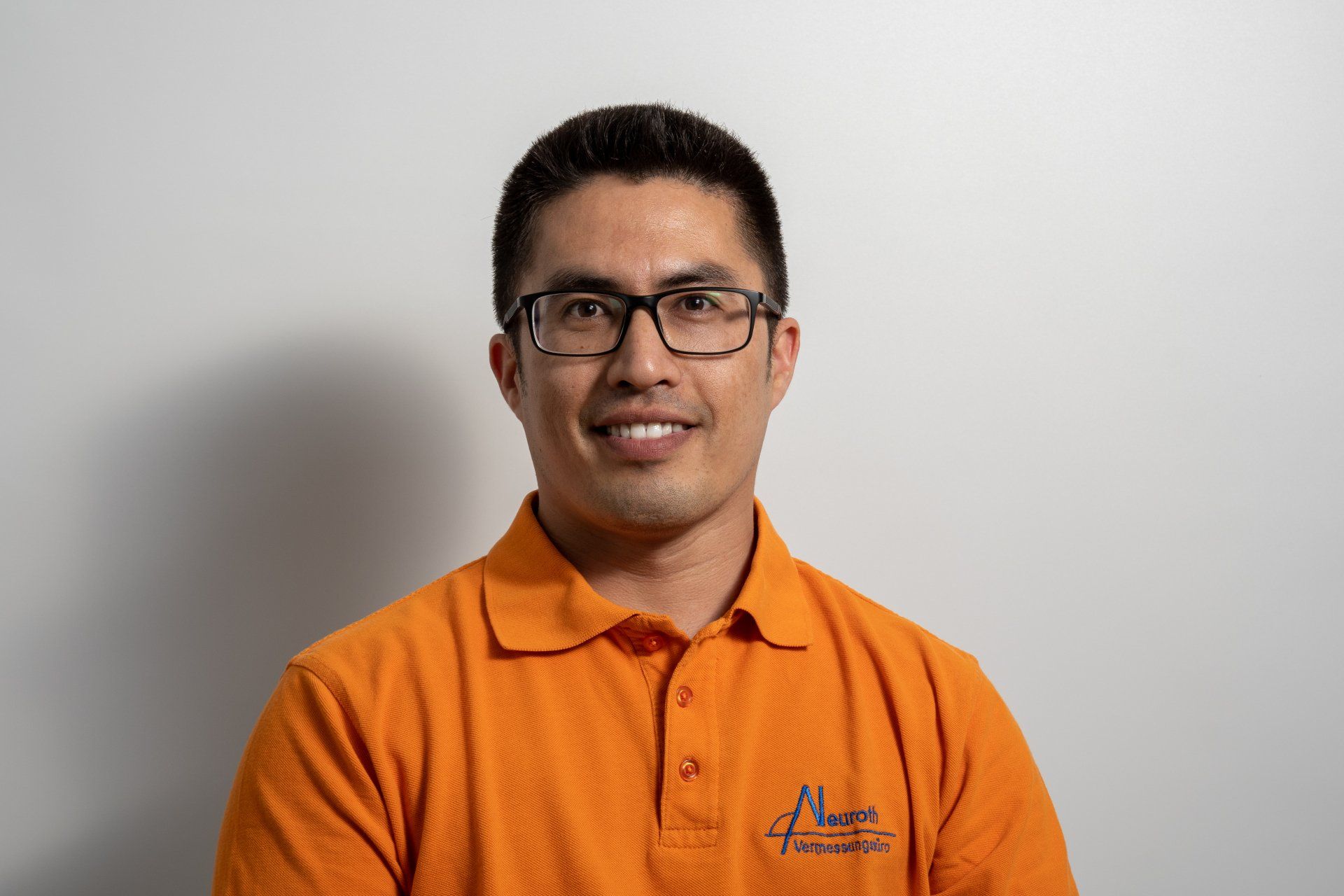 Ein Mann mit Brille und orangefarbenem Poloshirt lächelt in die Kamera.