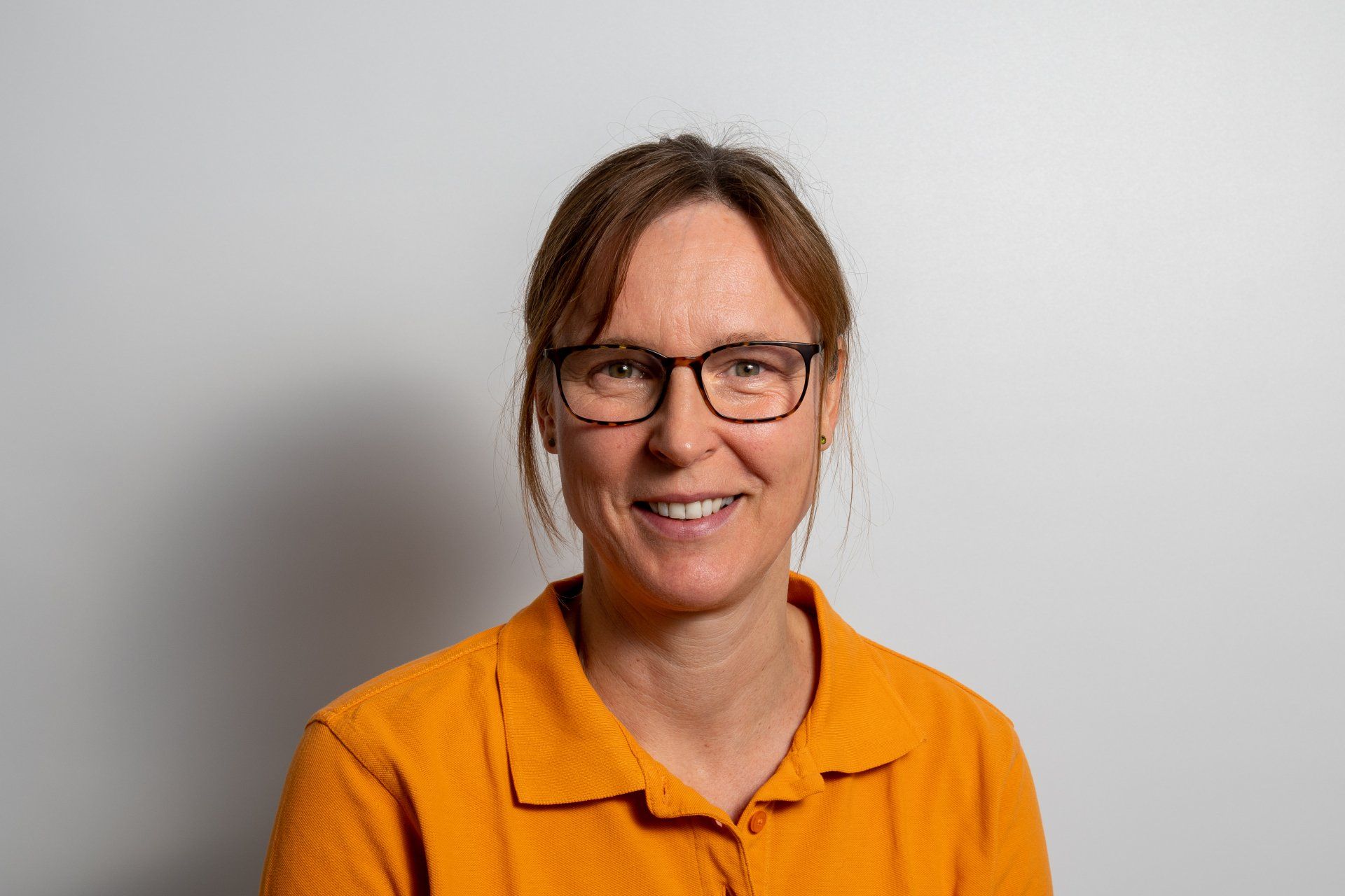Eine Frau mit Brille und orangefarbenem Hemd lächelt in die Kamera.