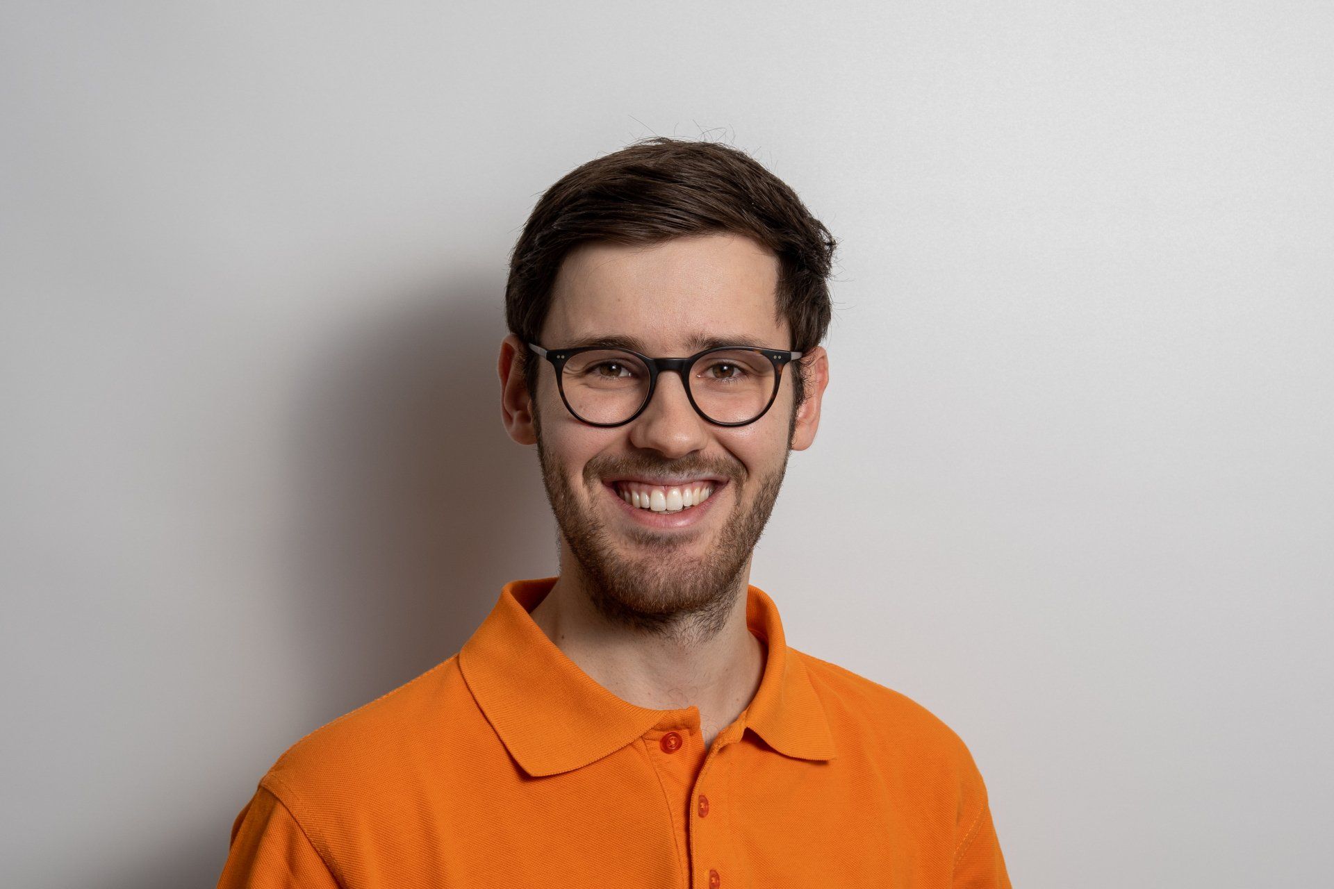 Ein Mann mit Brille und orangefarbenem Poloshirt lächelt in die Kamera.