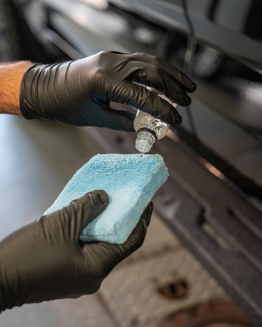 A person wearing black gloves is polishing a black car