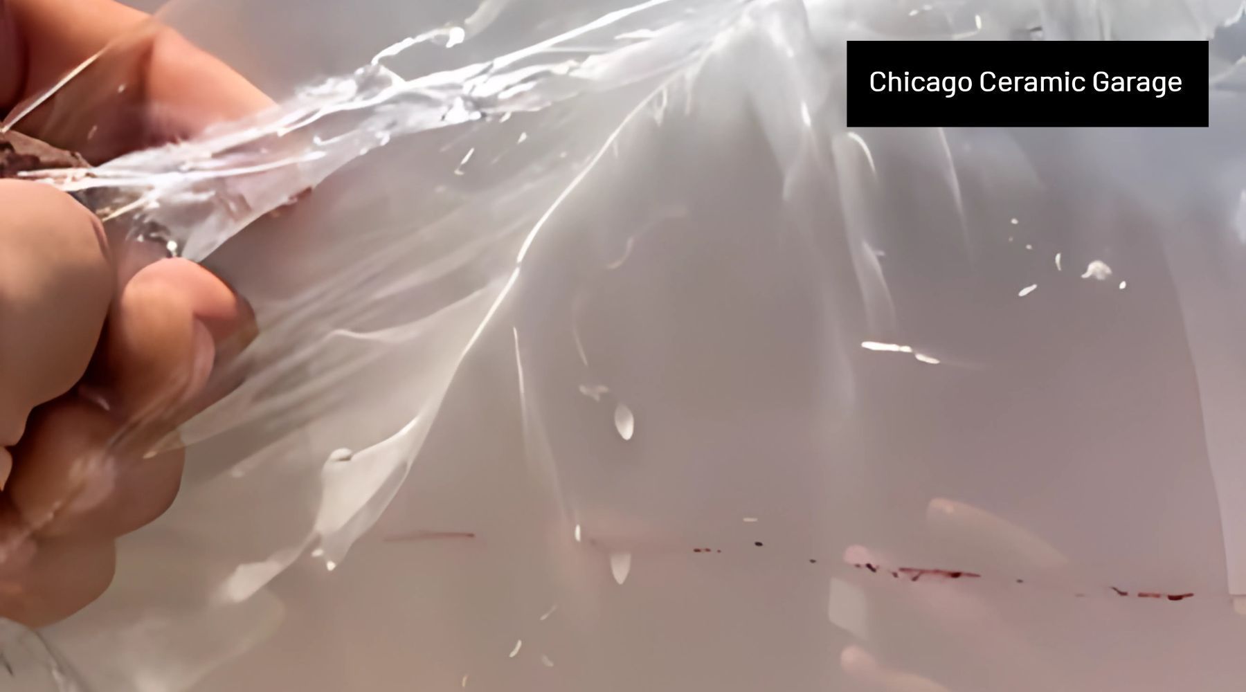 A hand pulling back a transparent layer of paint protection film from a car surface, showing water d